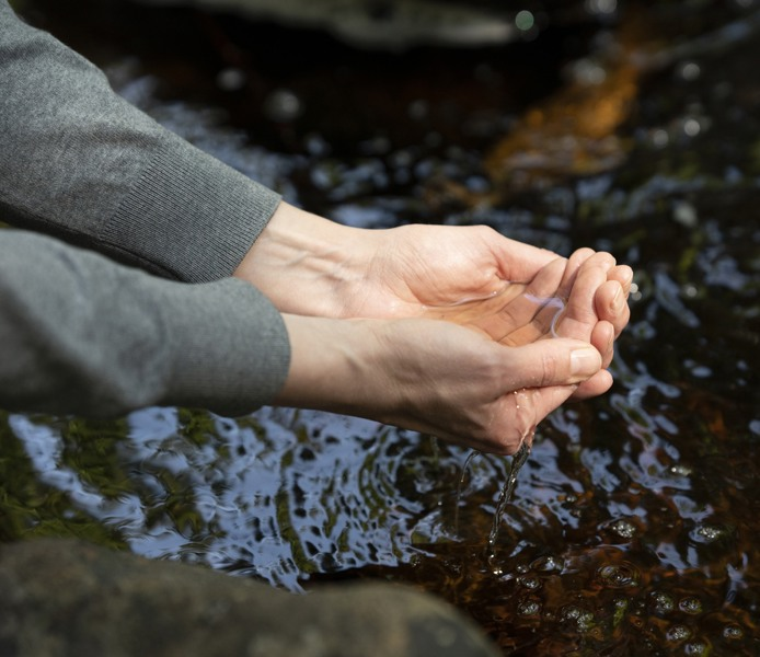 Händer som lyfter vatten ur ett vattendrag.