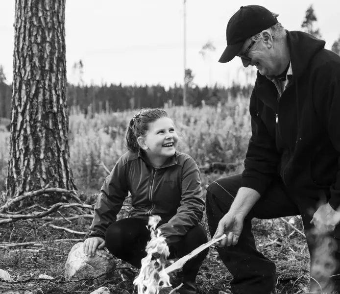 Ung flicka och äldre man sitter vid en eld