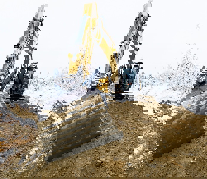 Grävskopa flyttar sand och jord med sin skopa på vintern.